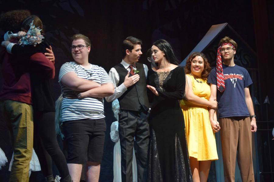From left to right: Lucas (One Griffin), Pugsley (Jacob Shaffer), Gomez (Bryce Craig), Morticia (Olivia Hsu), Alice (Sophia Chavez), Mal (Nick Leach). The Addams Family and Beineke family watch in glee as Lucas and Wednesdays hug each other.