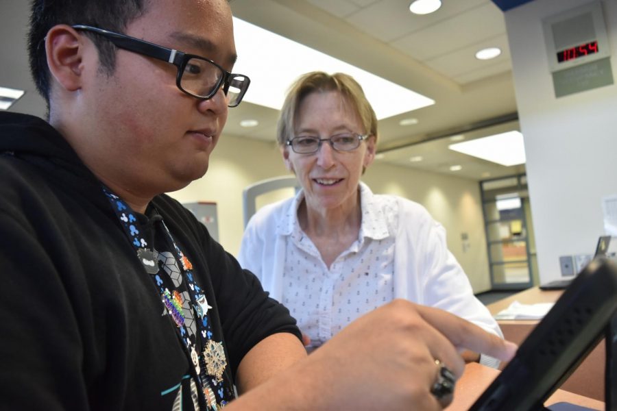 Frank Nguyen, senior and library TA, works with Gail Salameh to fix the wifi on his iPad.