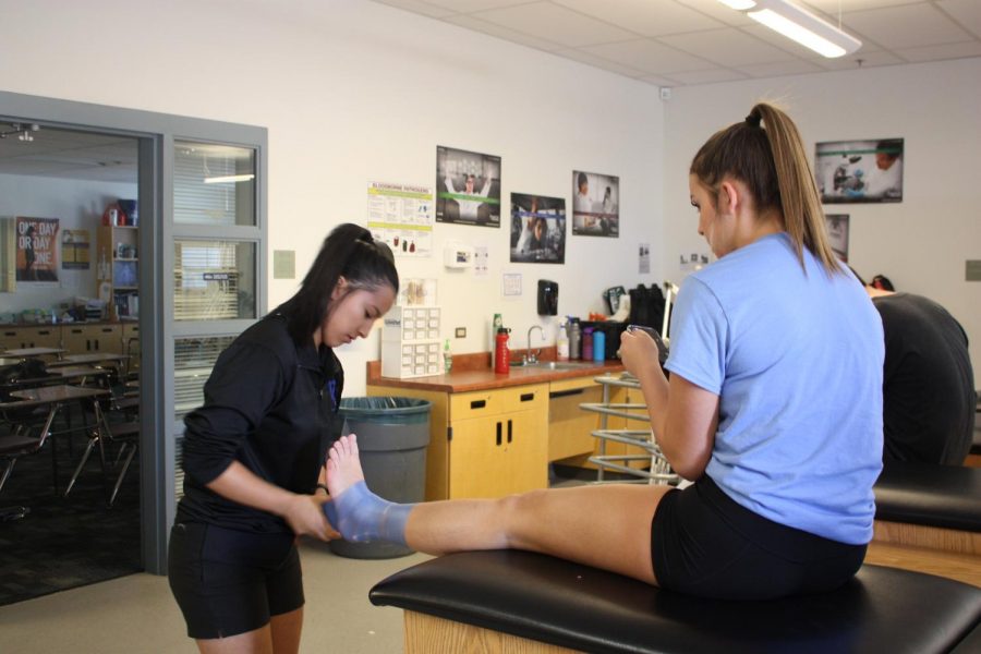 Student intern wraps up athlete’s ankle in between practices.