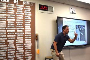 Uriah Cross, history teacher, gives a lecture next to his Wall of Fives.